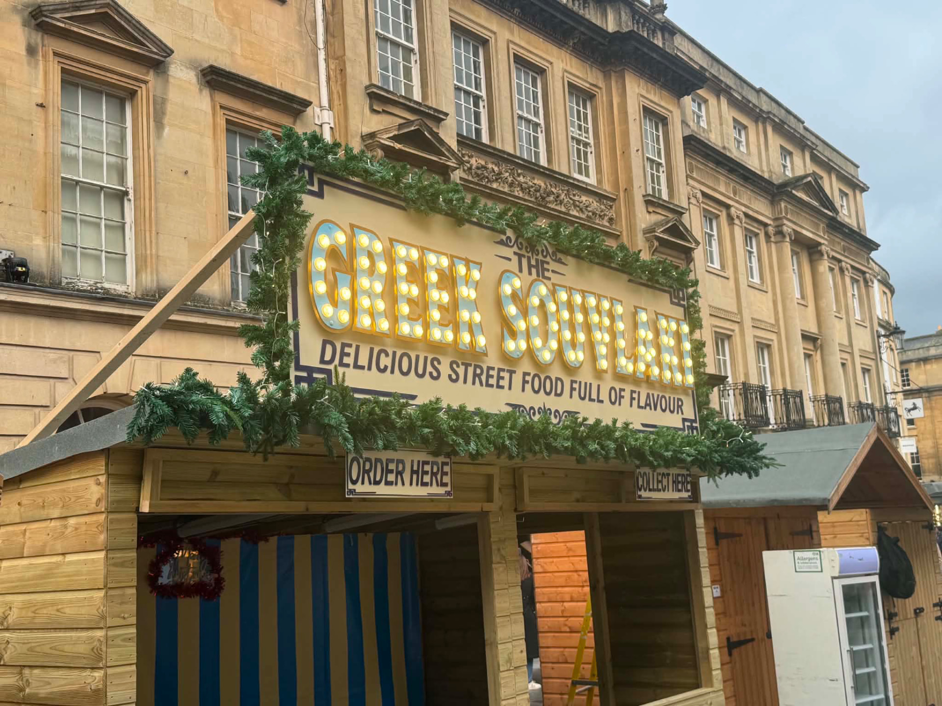 The Greek Souvlaki Christmas chalet with an illuminated top sign and festive garland surround