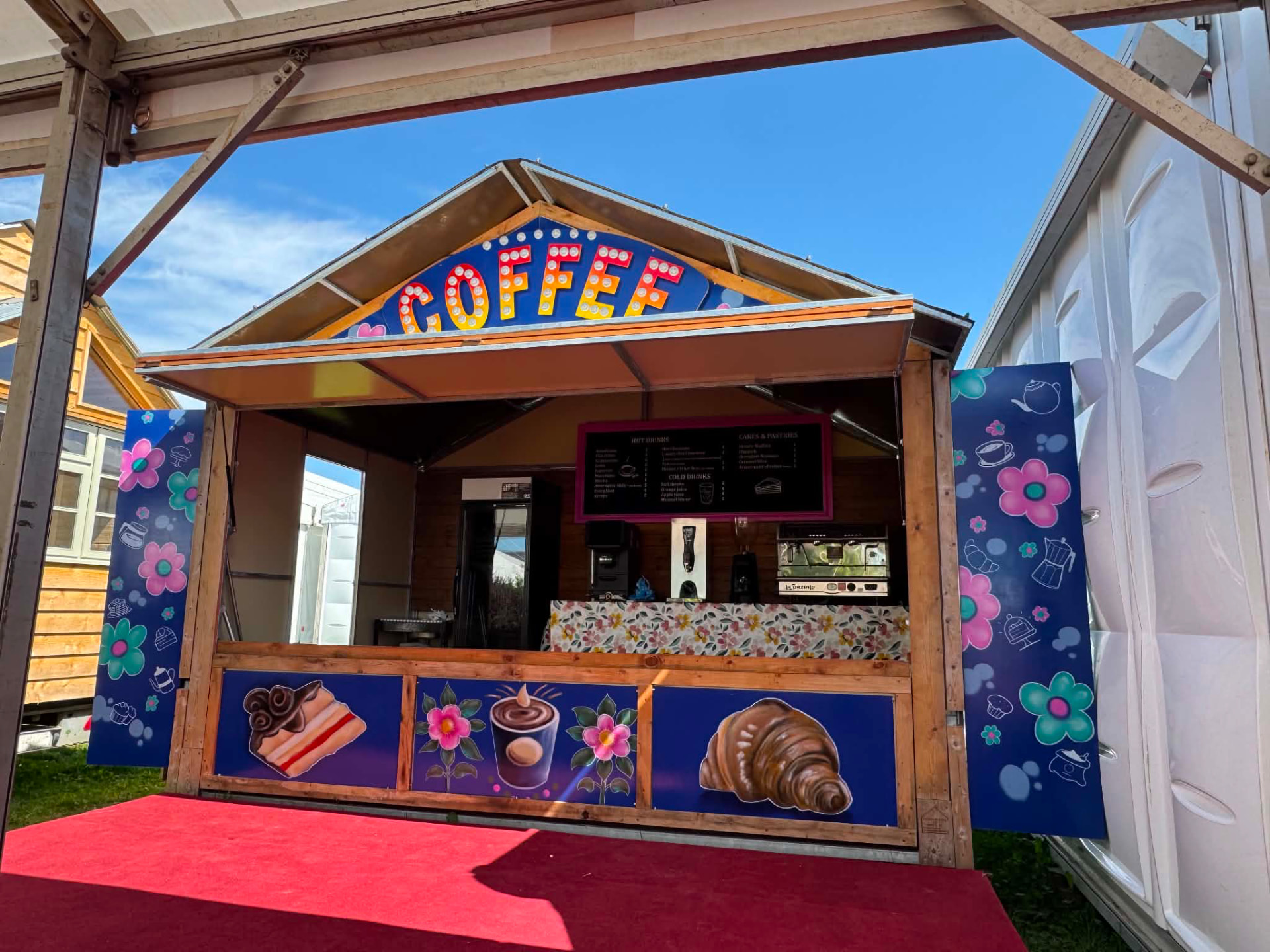 Wooden coffee chalet with illuminated COFFEE sign, printed menu and floral branded panels